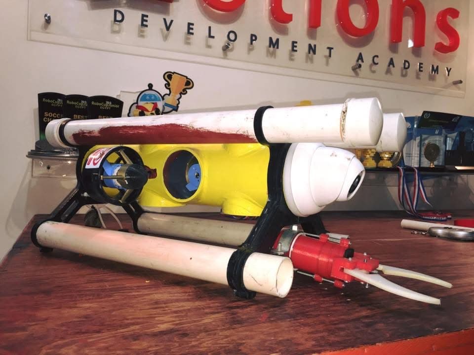 Our first remotely operated underwater vehicle, with a yellow body, white tubes and thrusters, on a worktable